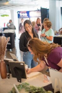 2 women are standing in the event and writing something on the paper